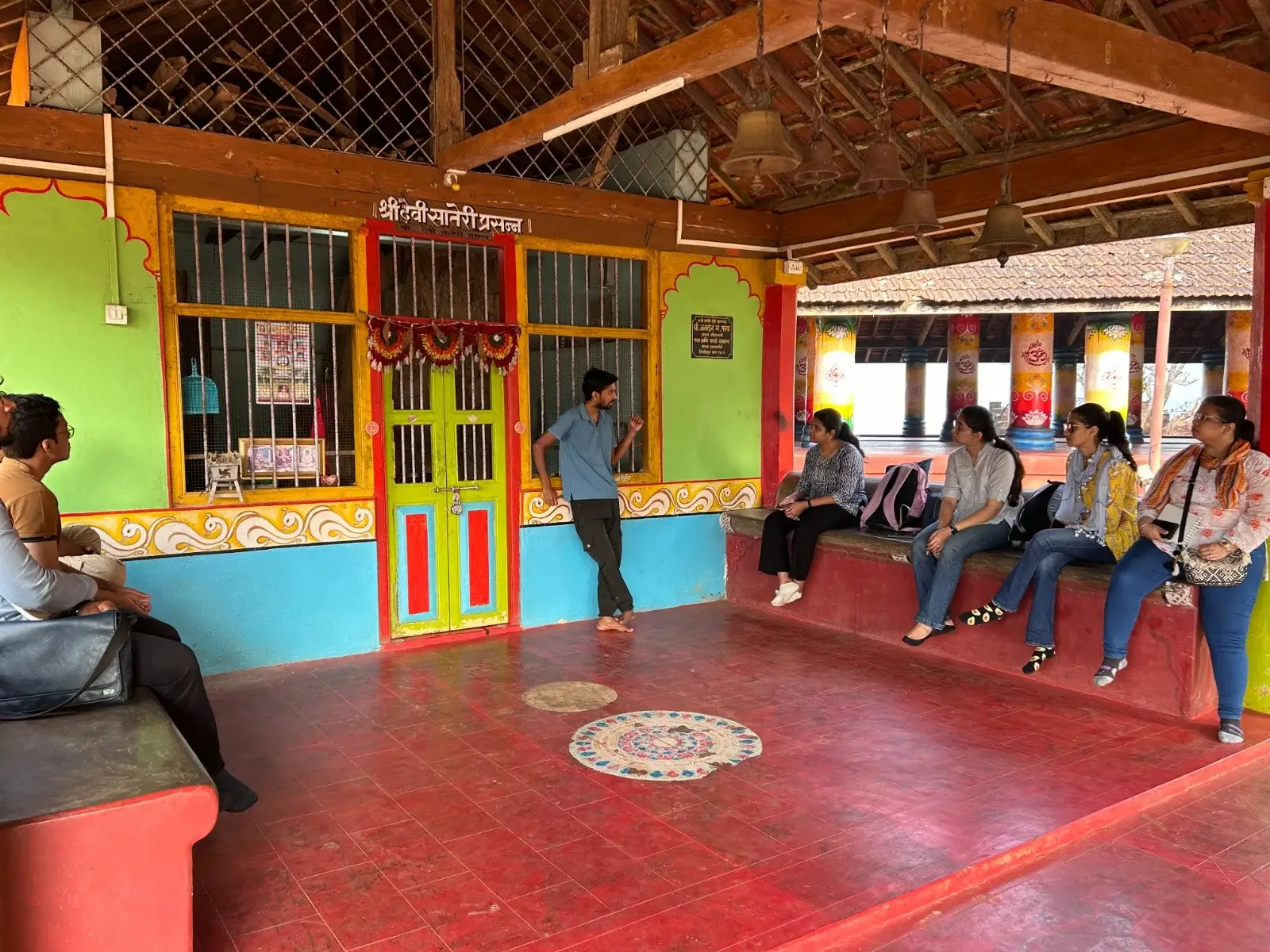 A group of participants seated inside a traditional temple courtyard, listening to a guide explain local culture and heritage in a colorful rural setting.